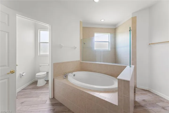 Primary Bathroom with tiled bath, toilet, and wood-type flooring