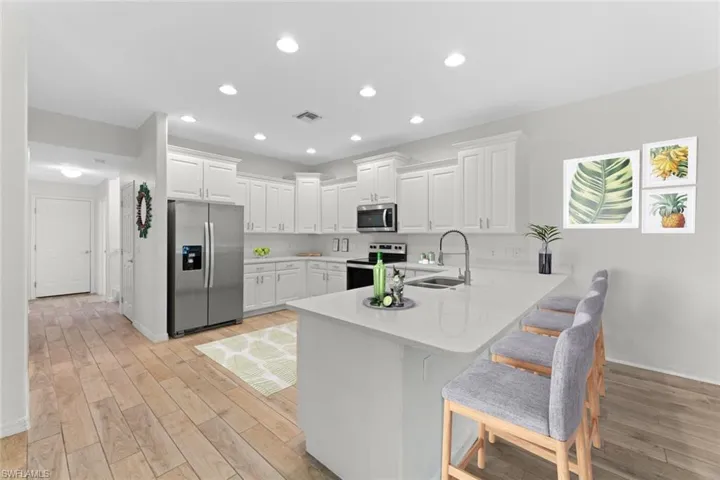 Virtually staged Kitchen featuring sink, light plank tile flooring, white cabinetry, and appliances with stainless steel finishes