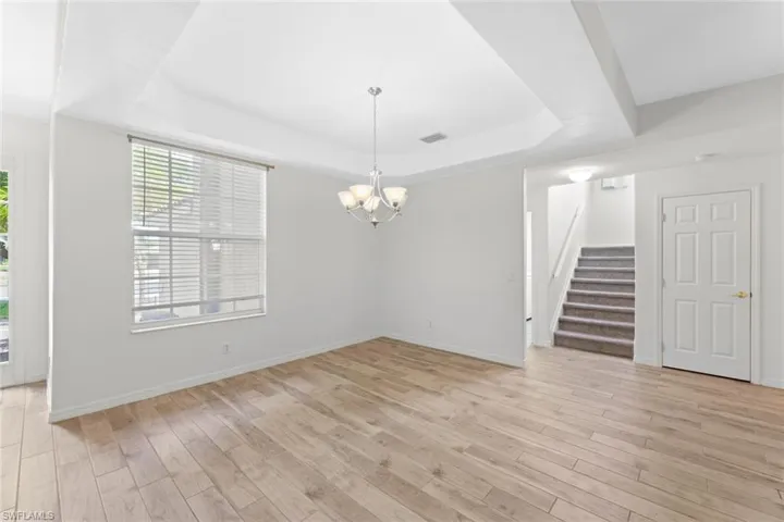 Dining area featuring an inviting chandelier, light hardwood / wood-style floors, and a raised ceiling