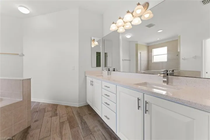 Primary Bathroom featuring a relaxing tiled bath, vanity with extensive cabinet space, dual sinks, and hardwood / wood-style floors