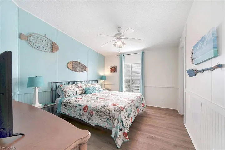 Bedroom featuring a textured ceiling, wood finished floors, ceiling fan, a decorative wall, and wainscoting