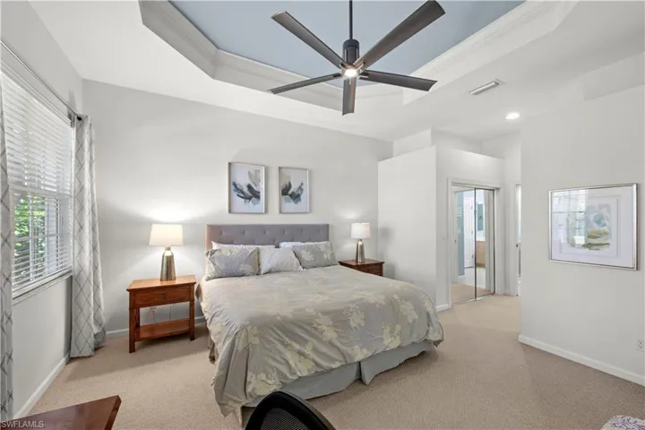 Bedroom featuring a raised ceiling, ornamental molding, light colored carpet, and a closet