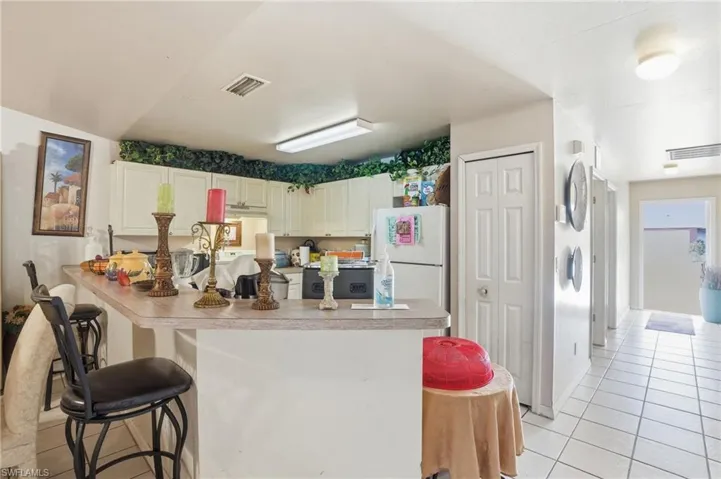 Kitchen featuring a kitchen bar, white cabinetry, light tile patterned floors, freestanding refrigerator, and light countertops