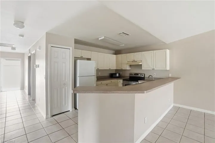 Kitchen with electric stove, light tile patterned floors, a peninsula, and freestanding refrigerator