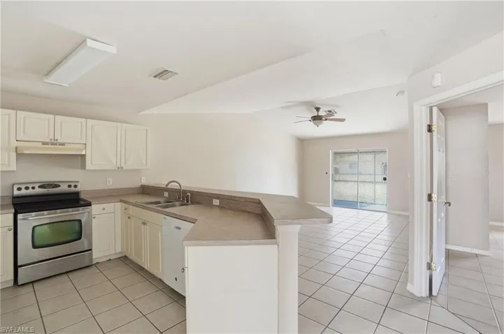 Kitchen with electric stove, a peninsula, ceiling fan, light tile patterned flooring, and vaulted ceiling