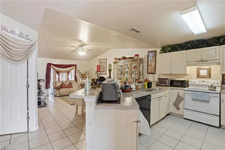 Kitchen featuring a peninsula, black appliances, light countertops, light tile patterned flooring, and lofted ceiling