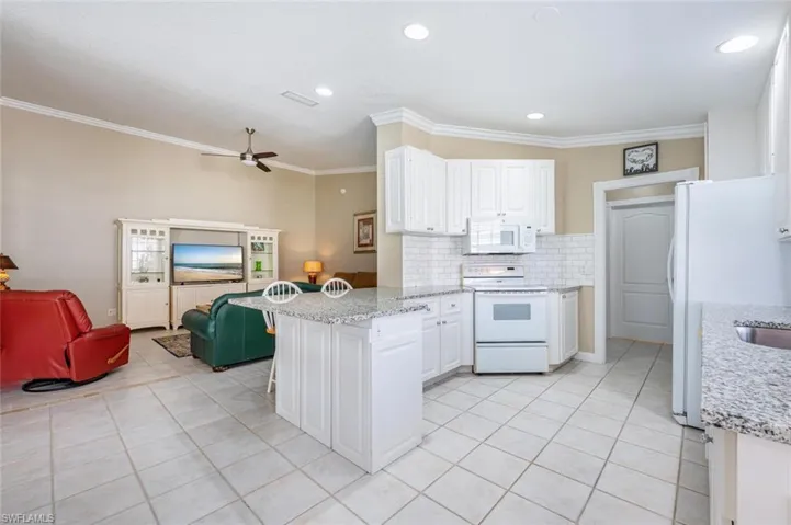 Kitchen featuring white appliances, decorative backsplash, light stone countertops, ceiling fan, and ornamental molding