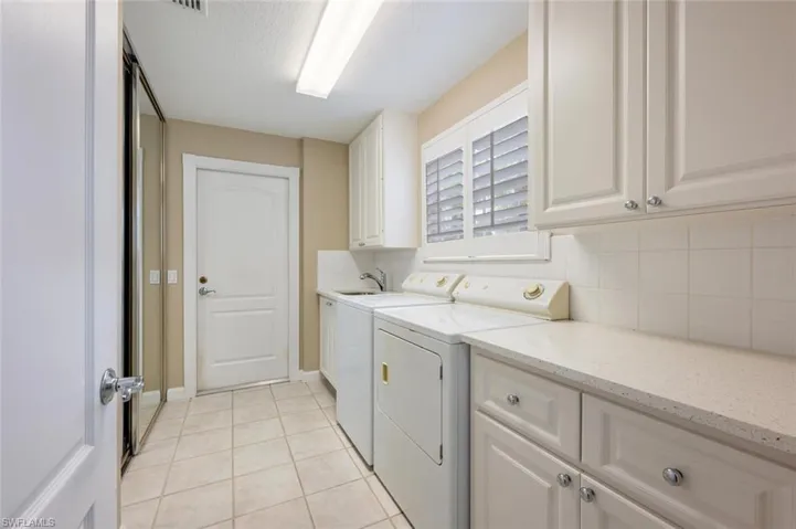 Washroom with sink, cabinets, light tile patterned floors, and washing machine and clothes dryer