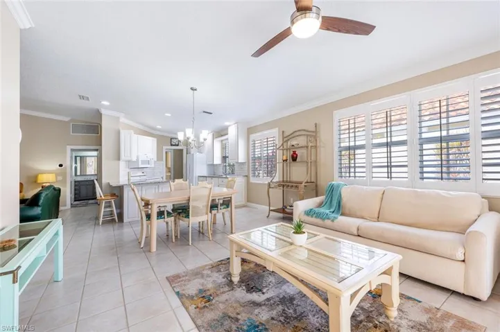 Living room featuring ornamental molding, ceiling fan with notable chandelier, and light tile patterned floors