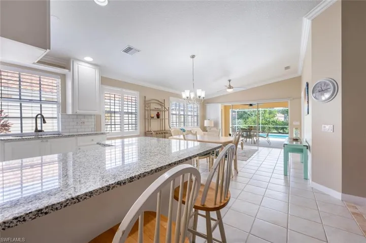 Kitchen featuring decorative light fixtures, white cabinets, a breakfast bar area, light stone countertops, and lofted ceiling