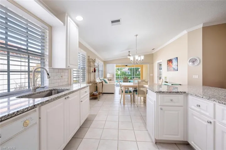 Kitchen featuring white dishwasher, sink, light tile patterned floors, white cabinetry, and ornamental molding