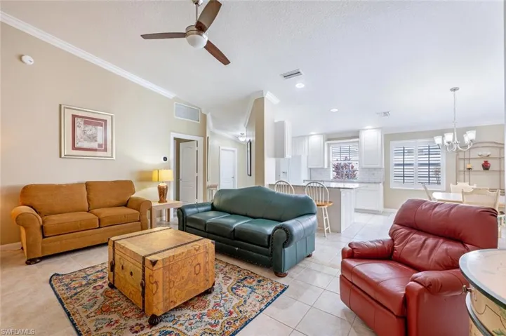 Living room featuring light tile patterned flooring, ceiling fan with notable chandelier, lofted ceiling, and ornamental molding