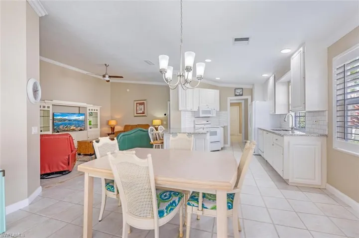 Dining space with light tile patterned flooring, crown molding, sink, and ceiling fan with notable chandelier