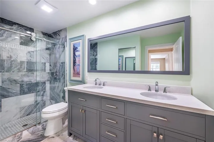 Bathroom featuring dual vanity, tile patterned floors, toilet, and an enclosed shower
