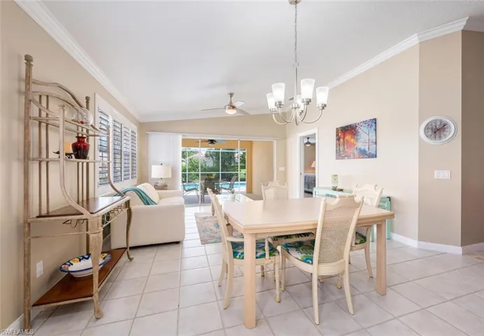 Dining area with ceiling fan with notable chandelier, lofted ceiling, crown molding, and light tile patterned floors
