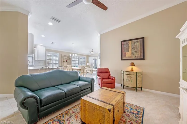 Living room featuring a textured ceiling, ceiling fan with notable chandelier, ornamental molding, and light tile patterned floors