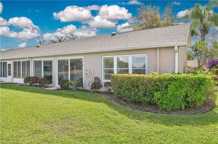 Rear view of property with a lawn, stucco siding, a sunroom, and roof with shingles