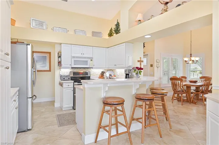 Kitchen with white cabinets, a breakfast bar area, stainless steel appliances, a chandelier, and tasteful backsplash