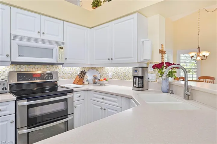 Kitchen with double oven range, white microwave, white cabinetry, and suspended lighting