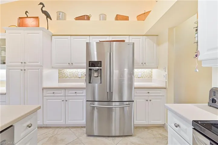 Kitchen with stainless steel refrigerator with ice dispenser, light countertops, tasteful backsplash, white cabinetry, and black / electric stove
