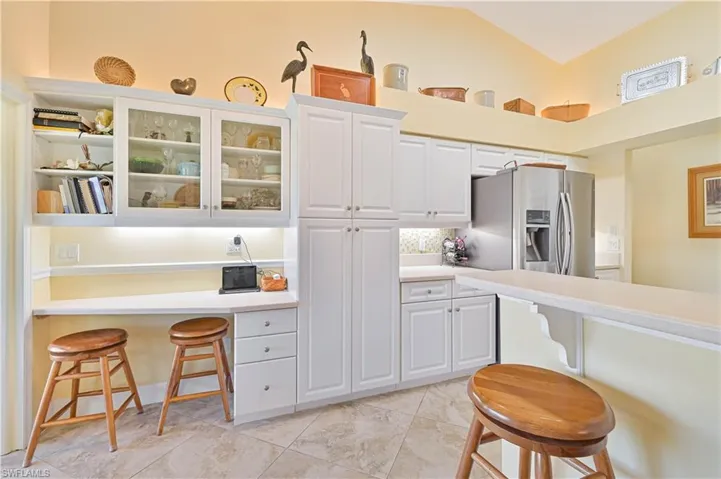 Kitchen featuring a kitchen breakfast bar, glass fronted cabinets, white cabinetry, backsplash, and vaulted ceiling