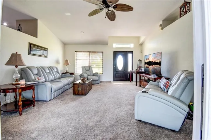 Carpeted living area with ceiling fan and lofted ceiling