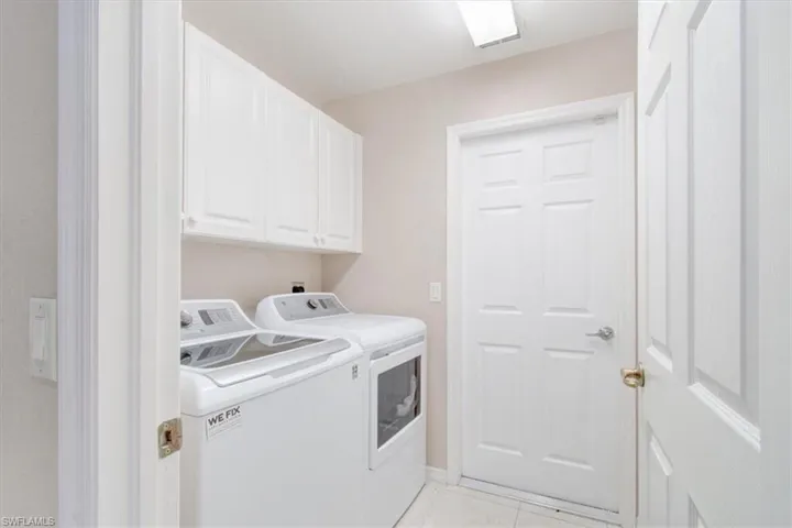 Laundry area featuring light tile patterned flooring, cabinet space, and washing machine and clothes dryer