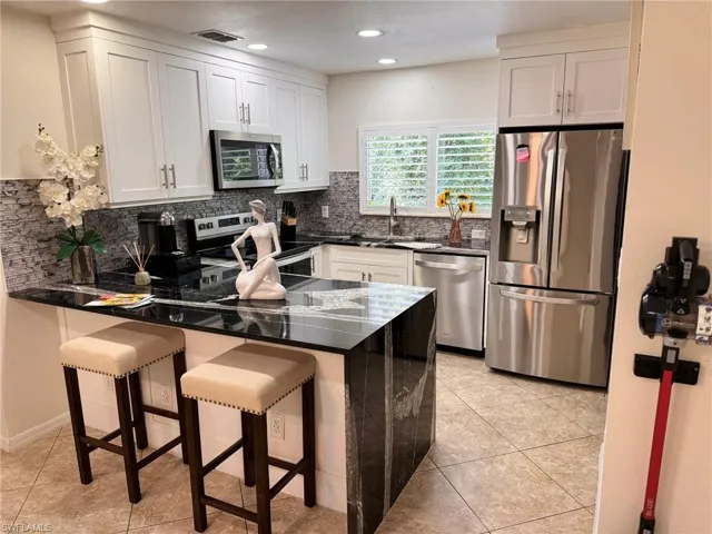 Kitchen with kitchen peninsula, backsplash, white cabinets, and stainless steel appliances