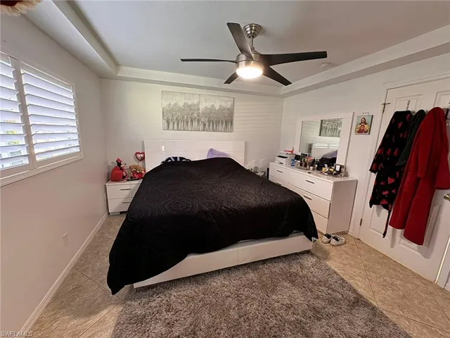 Bedroom featuring ceiling fan, light tile patterned flooring, and a raised ceiling