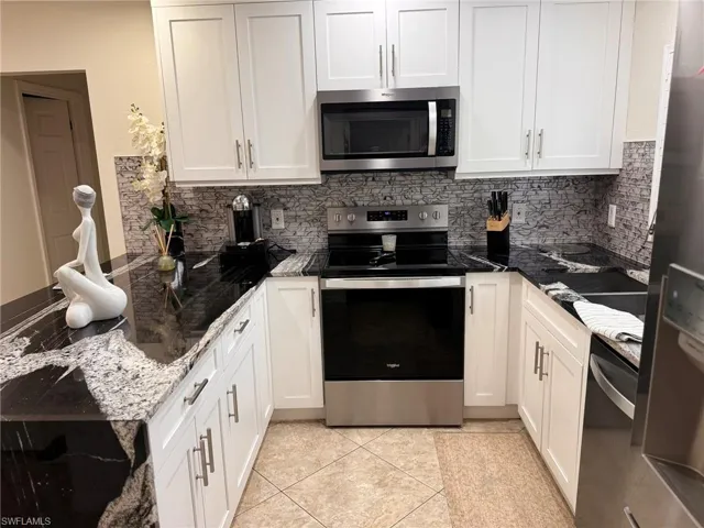 Kitchen with white cabinetry, appliances with stainless steel finishes, dark stone countertops, light tile patterned floors, and backsplash