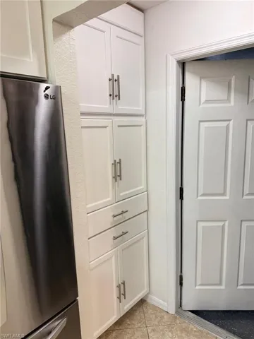 Kitchen with light tile patterned floors, white cabinetry, and stainless steel refrigerator