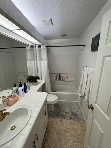 Full bathroom featuring a textured ceiling, shower / tub combo with curtain, toilet, vanity, and tile patterned flooring