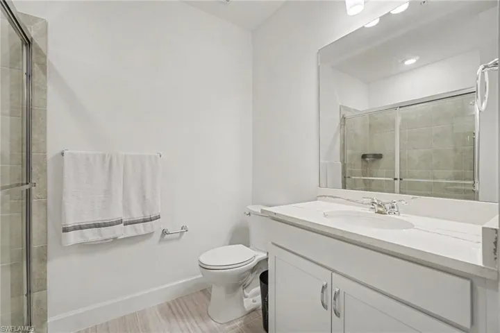 Bathroom featuring a vanity with a white countertop and undermount sink, a large mirror, a shower with sliding glass doors and tiled surround, and wood-finish flooring