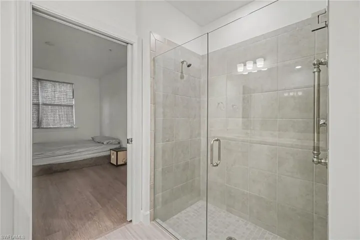Glass-enclosed shower featuring light grey wall tiling and a tiled shower pan