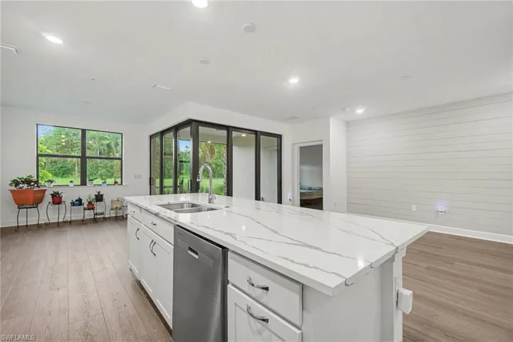 Kitchen island featuring a white countertop with veining, an undermount sink with a gooseneck faucet, a built-in dishwasher, and white cabinetry