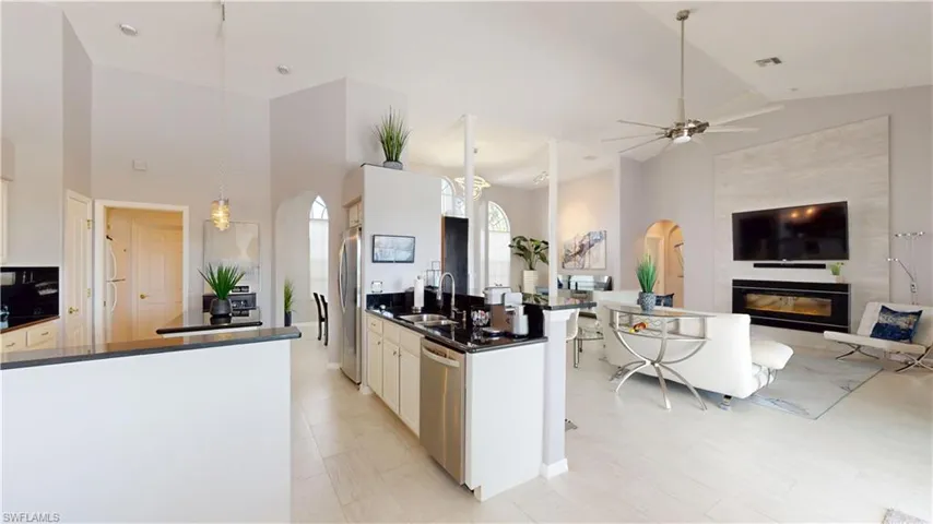 Kitchen with arched walkways, open floor plan, white cabinets, a fireplace, and vaulted ceiling