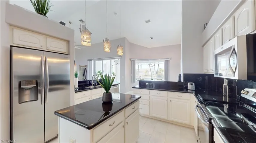 Kitchen with stainless steel appliances, a kitchen island, a peninsula, pendant lighting, and dark stone counters