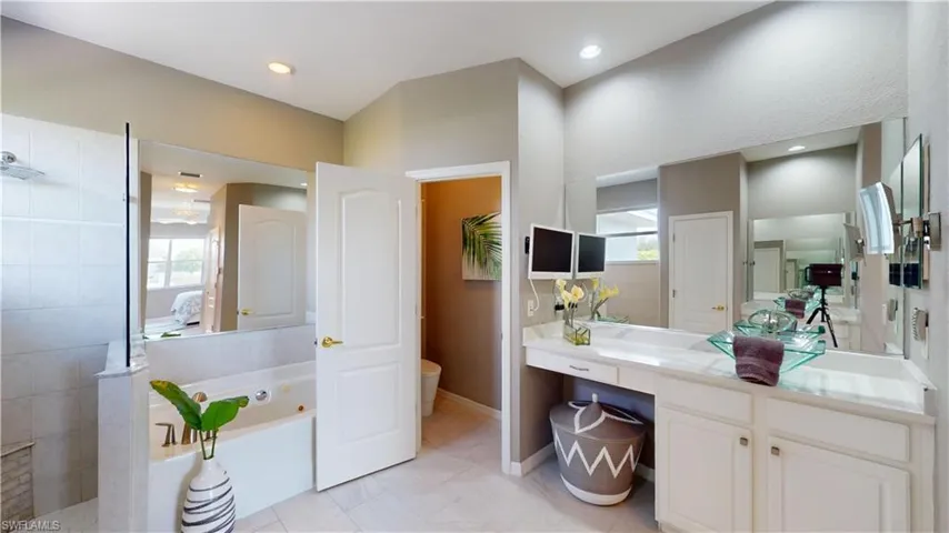 Ensuite bathroom featuring vanity, a tub with jets, walk in shower, and plenty of natural light