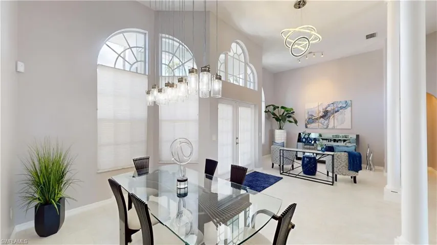 Dining space featuring ornate columns, hanging lights, healthy amount of natural light, a high ceiling, and french doors