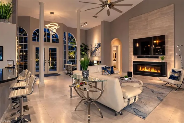 Living room featuring french doors, arched walkways, a tile fireplace, a ceiling fan, and suspended lighting