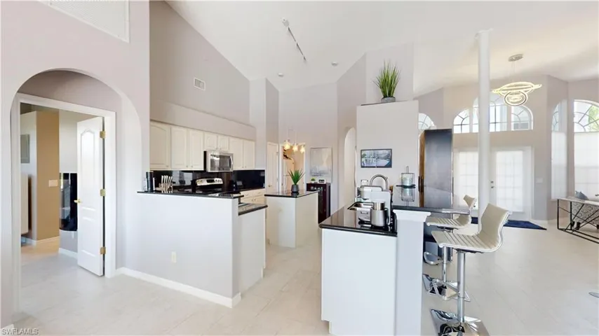 Kitchen with arched walkways, a kitchen breakfast bar, white cabinets, stainless steel microwave, and a peninsula