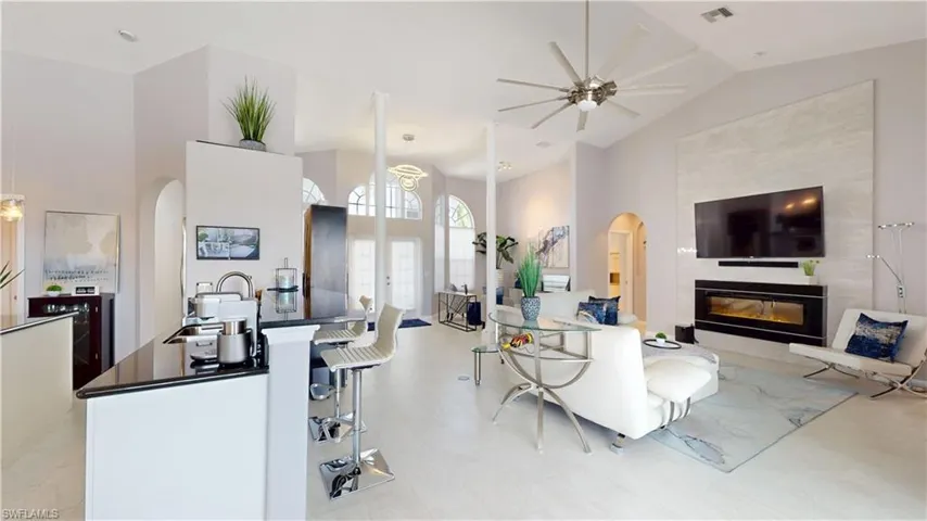 Living area featuring a tile fireplace, arched walkways, lofted ceiling, and ceiling fan