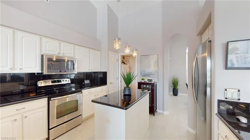 Kitchen with stainless steel appliances, a center island, a high ceiling, white cabinetry, and dark stone countertops