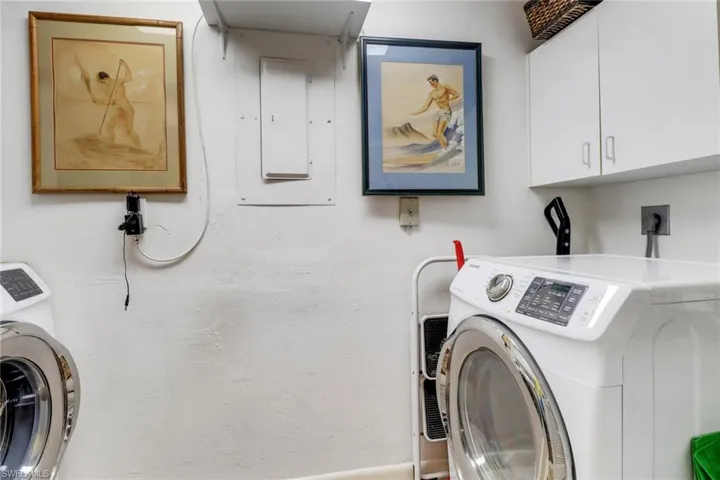 Clothes washing area with electric panel, cabinets, and washer / dryer