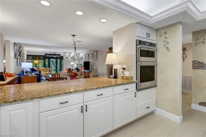 Kitchen with stainless steel double oven, light stone countertops, hanging light fixtures, white cabinets, and a chandelier