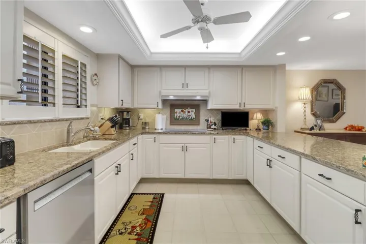 Kitchen featuring stainless steel dishwasher, white cabinets, sink, and a raised ceiling