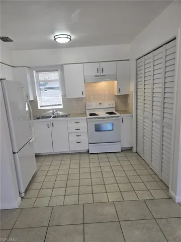 Kitchen with white cabinets, white appliances, light countertops, and backsplash