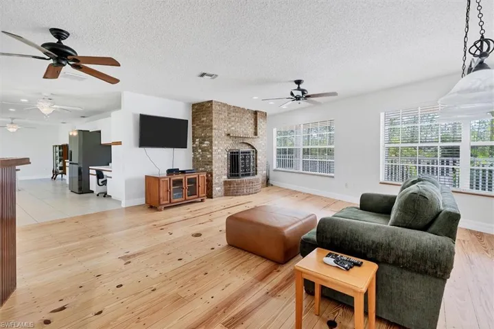 Living room with a fireplace, light hardwood / wood-style floors, a textured ceiling, and ceiling fan