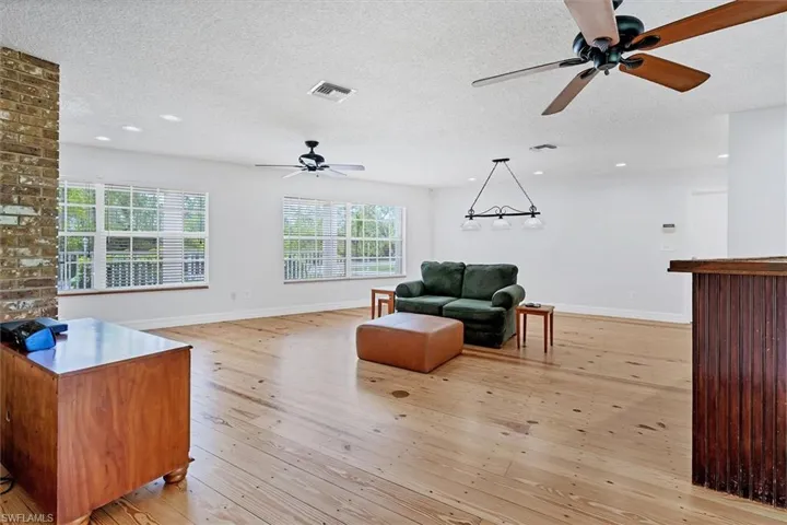 Living room featuring brick wall, light wood-type flooring, ceiling fan, and a textured ceiling