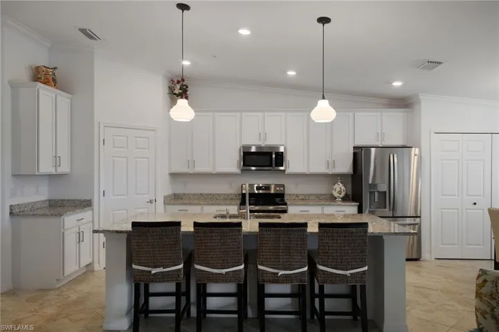 Kitchen featuring appliances with stainless steel finishes, hanging light fixtures, white cabinetry, vaulted ceiling, and a center island with sink